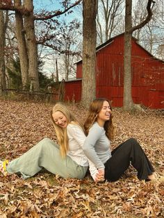 two young women sitting on the ground in front of some trees and leaves, smiling at the camera