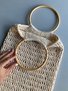 a crocheted bag with a wooden ring on the handle is held up by a woman's hand