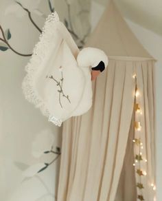 a stuffed swan hanging from the side of a bed in a room with white curtains and lights