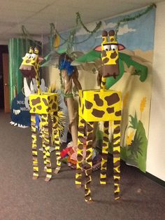 three paper mache giraffes standing in front of a wall with paintings on it