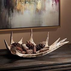 a bowl filled with pine cones sitting on top of a wooden table next to a painting