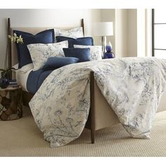 a bed with blue and white comforters in a bedroom next to a lamp on a table