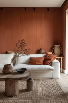 a living room with a couch, table and vases on the floor in front of an orange wall