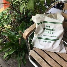 a white bag sitting on top of a wooden bench next to green plants and trees