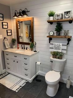 a white bathroom with black and white accessories on the shelves above the toilet is decorated with potted plants