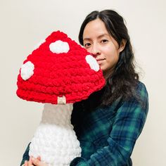 a woman holding a crocheted mushroom pillow in front of her face and looking at the camera