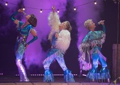 three women in blue and silver outfits performing on stage with lights behind them at night