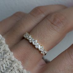 a woman's hand wearing a gold ring with three stones on it and a white sweater in the background