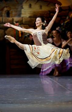 a woman in a brown and white dress is doing a ballet move with her legs spread out