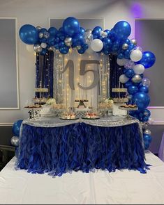 a table topped with blue and white balloons next to a number 15 cake on top of a table