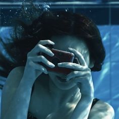 a woman in black swimsuit holding up her cell phone to her face under water