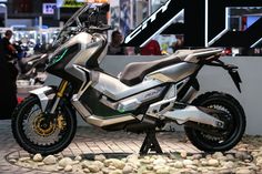 a silver motorcycle parked on top of a stone floor next to a building with people looking at it