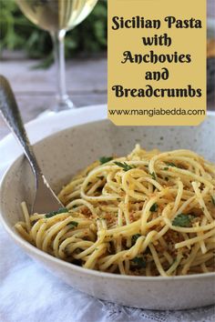 pasta with anchovies and breadcrumbs in a bowl next to two glasses of wine