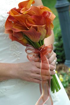 a bride holding a bouquet of orange flowers in her hands and wearing a white dress