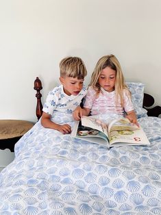 two children sitting on a bed reading a book