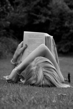 a woman laying on the grass reading a book with her legs crossed in front of her face