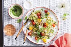 a white plate topped with pasta and veggies next to a bowl of pesto sauce