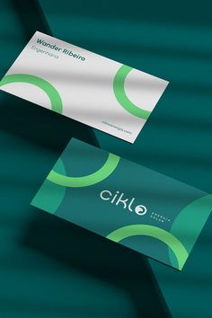 two business cards sitting next to each other on top of a green surface with the word ciklo printed on it