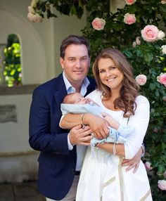 a man and woman holding a baby in front of a rose covered archway with pink flowers