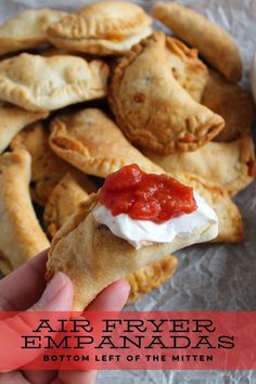 a hand holding up a piece of empanada with sauce on it and the text air fryer empanadas bottom left of the mitten