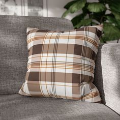 a brown and white plaid pillow sitting on top of a gray couch next to a potted plant