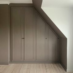 an empty room with wooden floors and gray cupboards in the corner, under a slanted ceiling