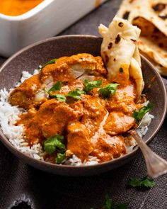 a bowl filled with chicken curry and rice next to pita bread on a table