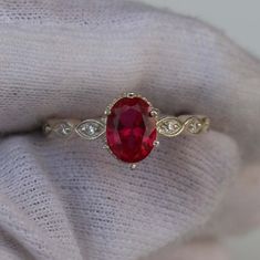 a close up view of a ring with a red stone in the middle and white diamonds around it