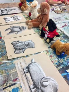 several stuffed animals sitting on top of a table next to some drawings and pencils