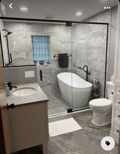 a bathroom with a tub, toilet and sink in the shower stall is seen through an open glass door