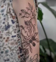 a woman's arm with an apple and bear tattoo on it, next to a potted plant