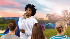 a man standing in front of a group of people on a field with tents behind him