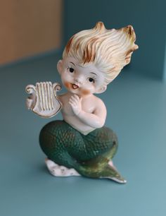 a little boy figurine sitting on top of a green and white mermaid tail