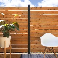 two white chairs sitting next to each other in front of a wooden fence with plants on it