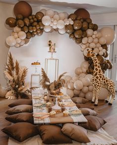 a giraffe standing next to a table filled with lots of balloons and decorations