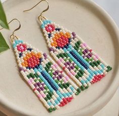 a pair of colorful beaded earrings sitting on top of a white plate next to a plant