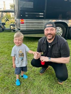 a man kneeling down next to a little boy on top of a grass covered field