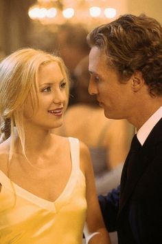 a woman in a yellow dress and a man in a black suit talking to each other