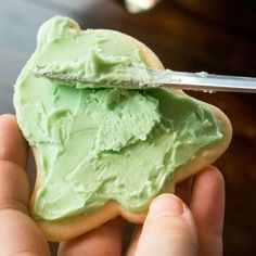 a hand holding a cookie with green frosting on it and a knife in the middle