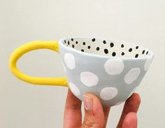 a hand holding a white and black polka dot coffee cup with yellow rubber band around it