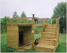 a dog house made out of wood with stairs leading up to the door and another dog standing on top of it