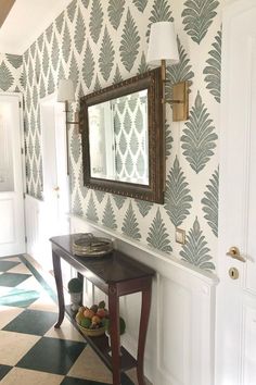 a hallway with wallpaper and a mirror on the wall above a table in front of a door