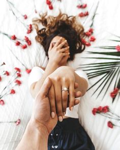 a man and woman holding hands while laying on a bed with red flowers in the background