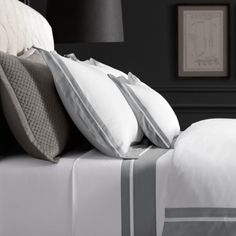 a bed with white and grey sheets and pillows on top of it next to a lamp