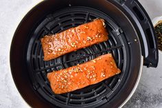 two salmons cooking in an air fryer with sesame seeds and seasoning on top