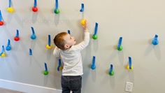 a little boy standing in front of a wall with colorful pegs on the wall