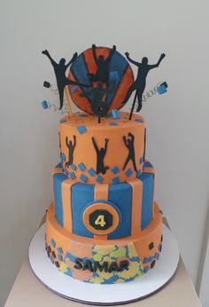 a three tiered cake with people on top and an orange blue and yellow design