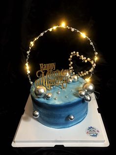 a blue birthday cake with pearls and lights on it's top is sitting on a white plate