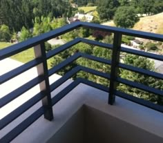 a balcony with black railings and trees in the background, looking down at a valley