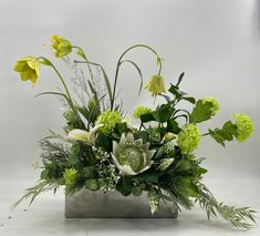 an arrangement of flowers and greenery in a vase on a white tablecloth background